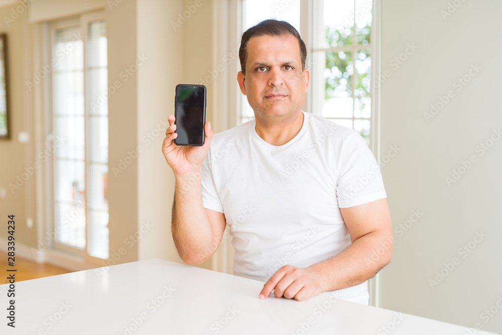 Middle age man showing smartphone screen with a confident expression on smart face thinking serious