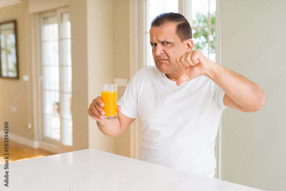 Middle age man drinking a glass of orange juice at home with angry face, negative sign showing dislike with thumbs down, rejection concept Middle age man drinking a glass of orange juice at home with angry face, negative sign showing dislike with thumbs down, rejection concept