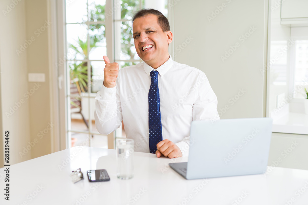 Middle age business man working with computer laptop smiling with happy face looking and pointing to the side with thumb up.