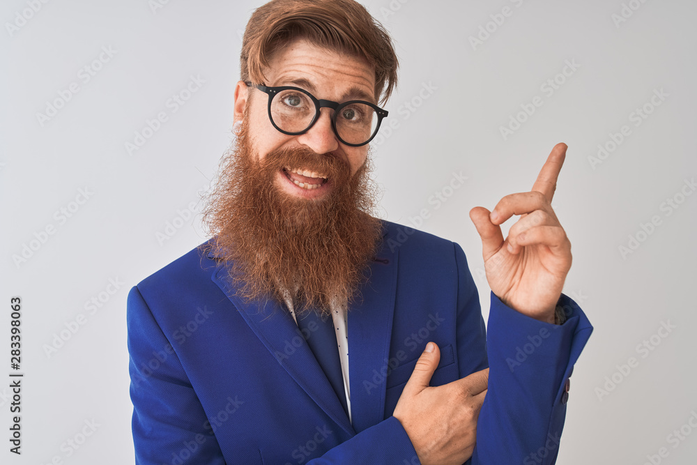 Young redhead irish businessman wearing suit and glasses over isolated white background with a big smile on face, pointing with hand and finger to the side looking at the camera. Young redhead irish businessman wearing suit and glasses over isolated white background with a big smile on face, pointing with hand and finger to the side looking at the camera.