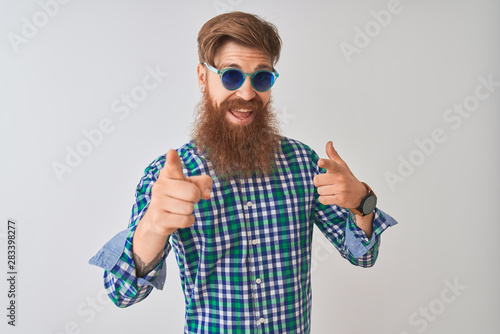 Young redhead irish man wearing casual shirt and sunglasses over isolated white background pointing fingers to camera with happy and funny face. Good energy and vibes.