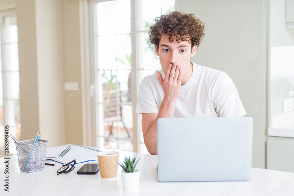 Young student man working and studying using computer laptop cover mouth with hand shocked with shame for mistake, expression of fear, scared in silence, secret concept Young student man working and studying using computer laptop cover mouth with hand shocked with shame for mistake, expression of fear, scared in silence, secret concept