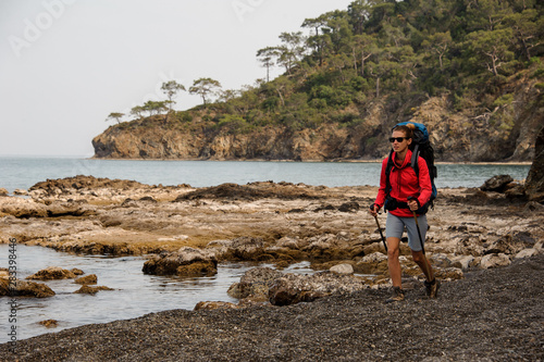 Sporty woman walking on the rocks on the sea with hiking backpack