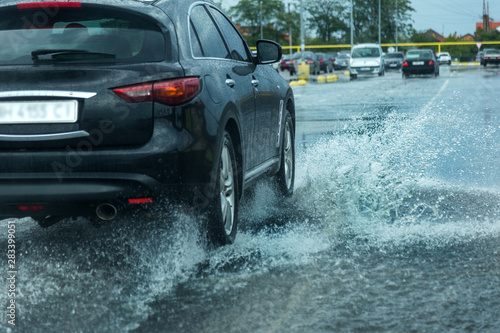Odessa, Ukraine - August 9, 2019: driving car on flooded road during flood caused by torrential rains. Cars float on water, flooding streets. Splash on the car. Flooded city road with a large puddle