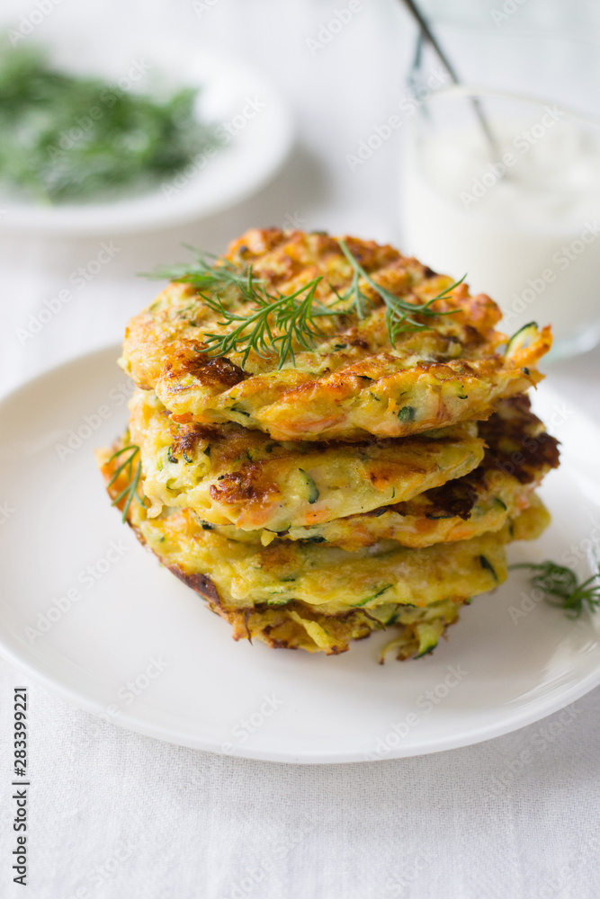 Zucchini, carrot, parmesan fritters on plate with dill and yogurt
