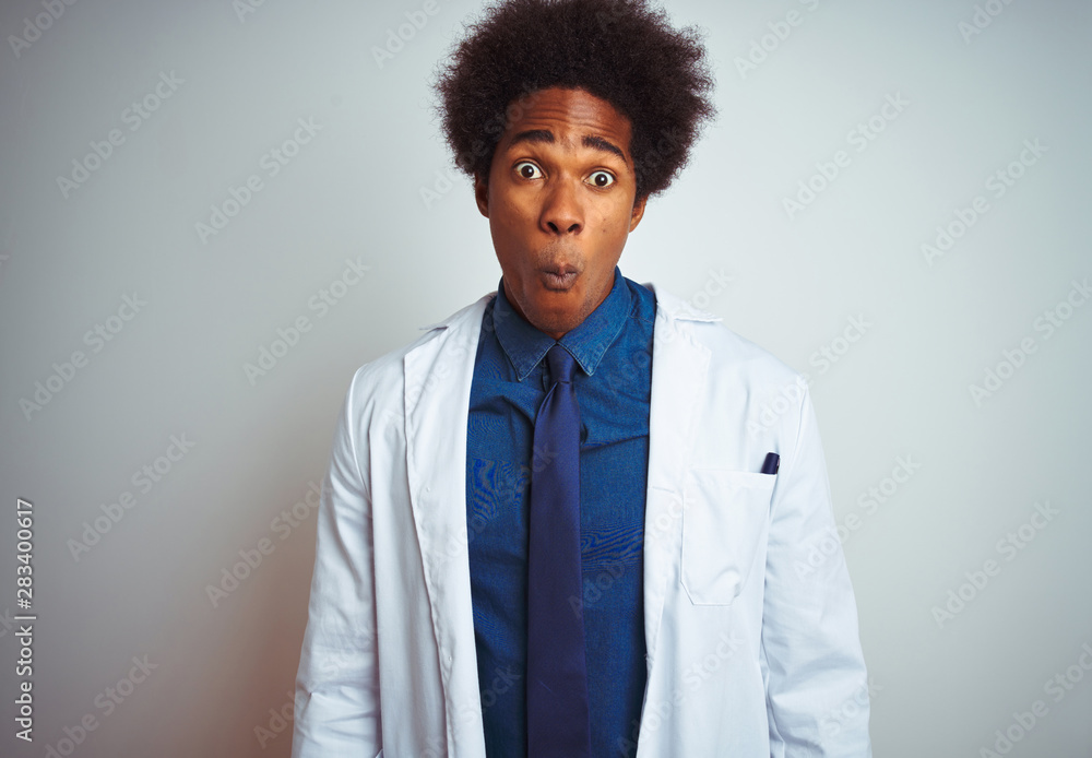 Young african american doctor man wearing coat standing over isolated white background making fish face with lips, crazy and comical gesture. Funny expression. Young african american doctor man wearing coat standing over isolated white background making fish face with lips, crazy and comical gesture. Funny expression.