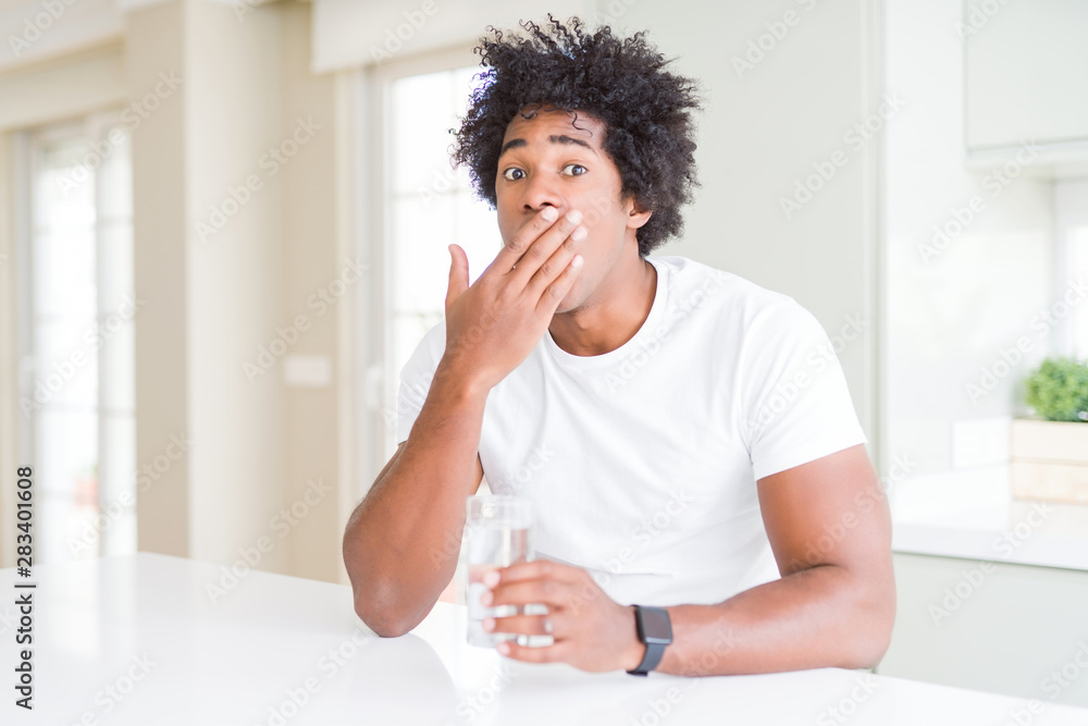 African American man drinking a glass of water at home cover mouth with hand shocked with shame for mistake, expression of fear, scared in silence, secret concept African American man drinking a glass of water at home cover mouth with hand shocked with shame for mistake, expression of fear, scared in silence, secret concept