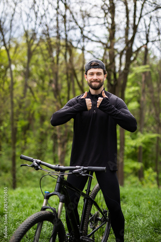 Happy man riding a mountain bike in the green woods.cyclist with ok symbol. Theme of sport and hiking. Cyclist in blue form in nature. Cyclist on the mountain bike in the forest.