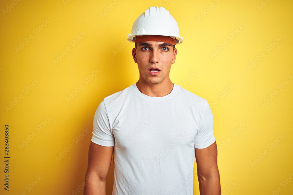 Young handsome man wearing construction helmet over yellow isolated background afraid and shocked with surprise expression, fear and excited face.