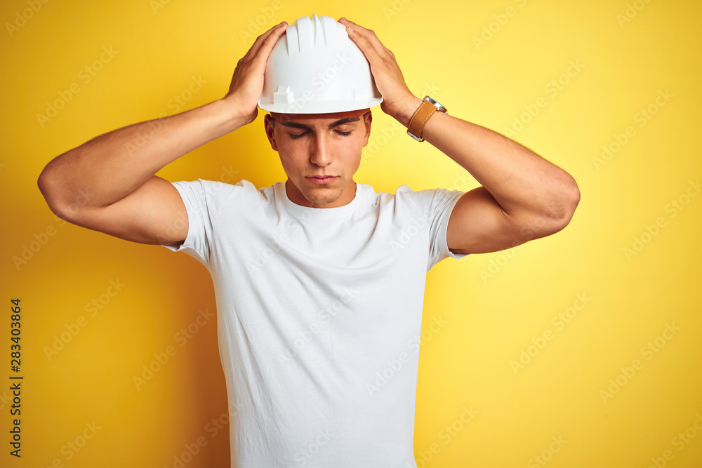 Young handsome man wearing construction helmet over yellow isolated background suffering from headache desperate and stressed because pain and migraine. Hands on head.