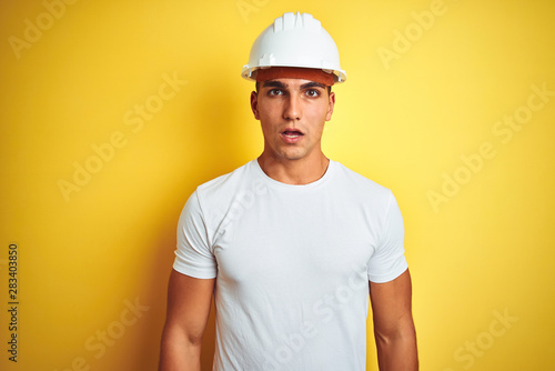 Young handsome man wearing construction helmet over yellow isolated background afraid and shocked with surprise expression  fear and excited face.