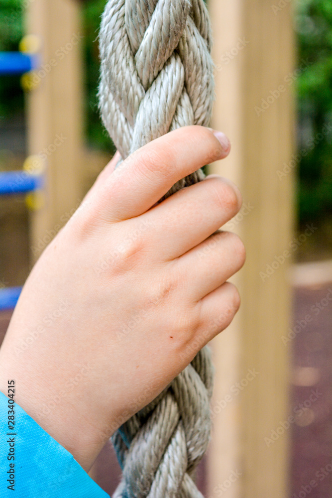 Child hand clings to thick rope for climbing of sports equipment