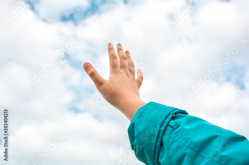 Close up of child hand raised up over blue sky and clouds background. Gesture