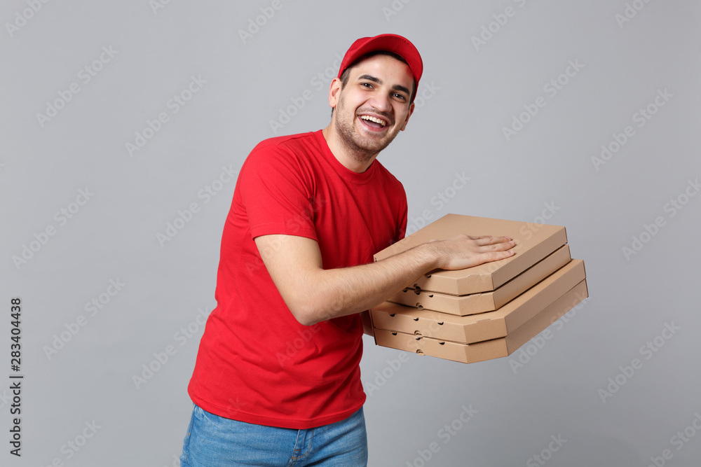 Delivery man giving hold food order pizza boxes isolated on grey background. Professional male pizzaman employee in red cap t-shirt print working as courier dealer. Service concept. Mock up copy space Delivery man giving hold food order pizza boxes isolated on grey background. Professional male pizzaman employee in red cap t-shirt print working as courier dealer. Service concept. Mock up copy space