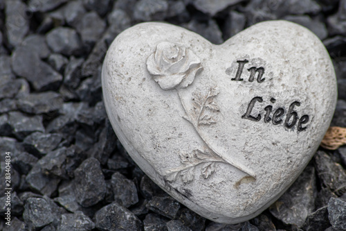 Weißes Steinherz mit Rose und Inschrift In Liebe auf einem Grab auf einem Friedhof als Andenken an liebe verstorbene Menschen, Eltern und Großeltern