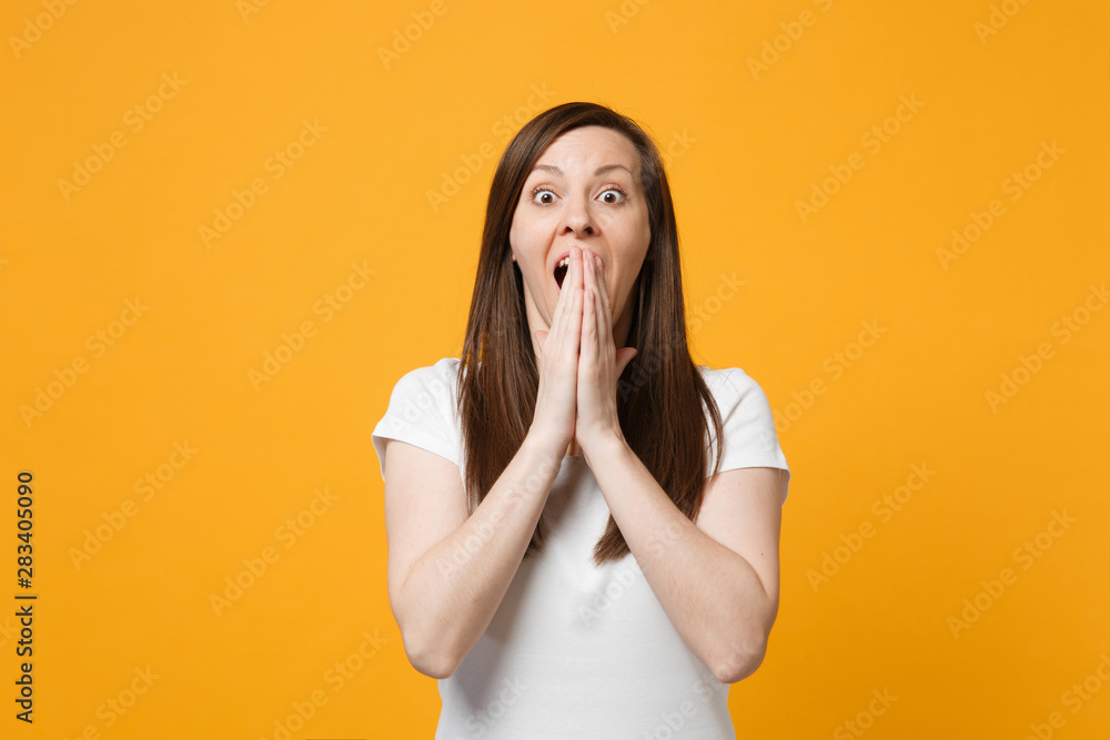 Portrait of shocked young woman in white casual clothes looking camera, covering mouth with hands isolated on bright yellow orange background in studio. People lifestyle concept. Mock up copy space. Portrait of shocked young woman in white casual clothes looking camera, covering mouth with hands isolated on bright yellow orange background in studio. People lifestyle concept. Mock up copy space.