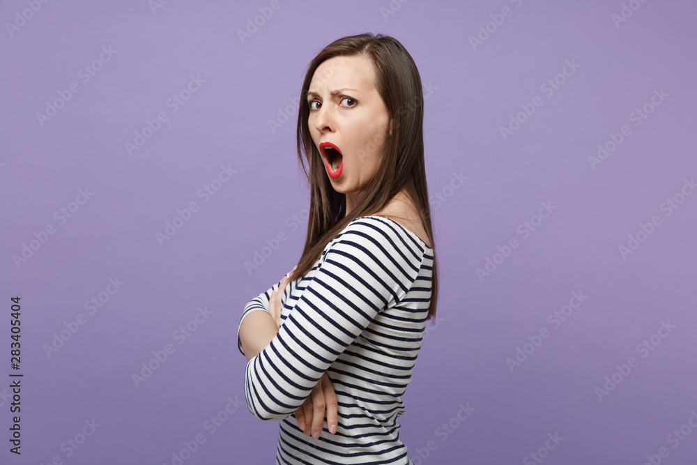 Side view of shocked irritated young woman in casual striped clothes posing isolated on violet purple background. People lifestyle concept. Mock up copy space. Holding hands folded keeping mouth open. Side view of shocked irritated young woman in casual striped clothes posing isolated on violet purple background. People lifestyle concept. Mock up copy space. Holding hands folded keeping mouth open.