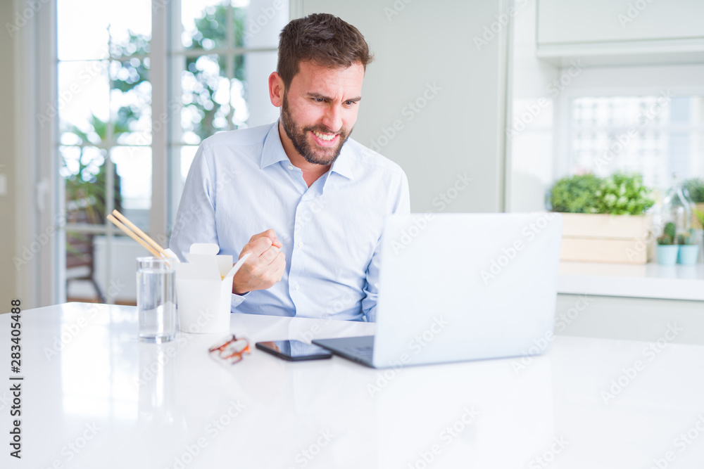 Business man eating take away asian noodles food while working using computer laptop and smiling
