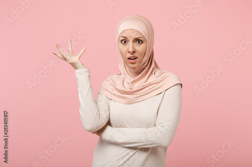 Bilde på lerret Perplexed bewildered young arabian muslim woman in hijab light clothes posing isolated on pink background studio portrait