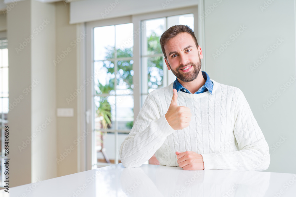 Handsome man wearing casual sweater doing happy thumbs up gesture with hand. Approving expression looking at the camera showing success.