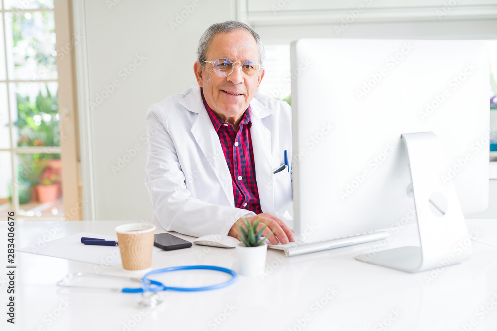 Senior doctor man at the clinic working with computer and smiling