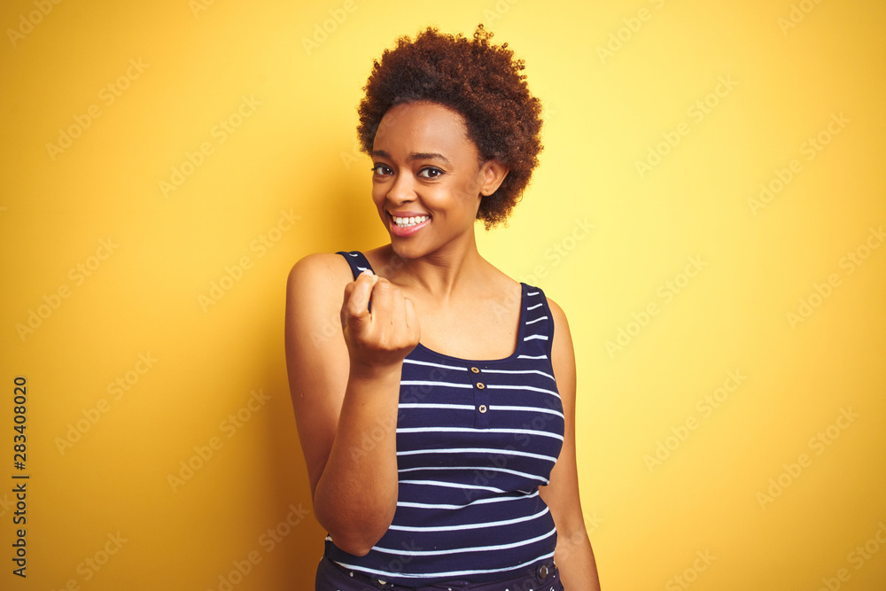 Beauitul african american woman wearing summer t-shirt over isolated yellow background Beckoning come here gesture with hand inviting welcoming happy and smiling Beauitul african american woman wearing summer t-shirt over isolated yellow background Beckoning come here gesture with hand inviting welcoming happy and smiling