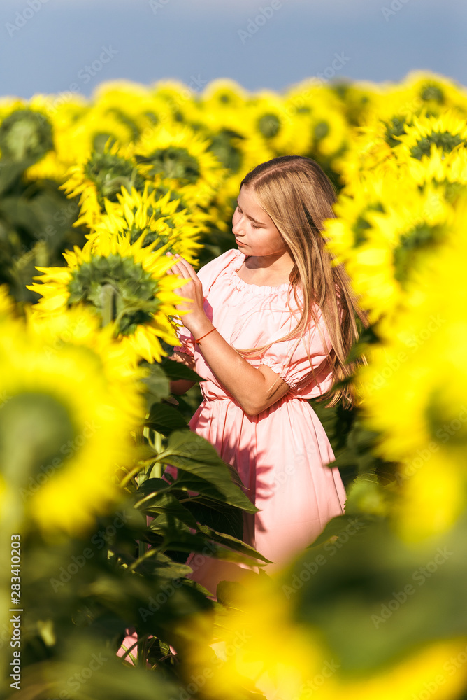 Pretty teen girl standing among sunflowers, posing for camera with eyes closed Pretty teen girl standing among sunflowers, posing for camera with eyes closed
