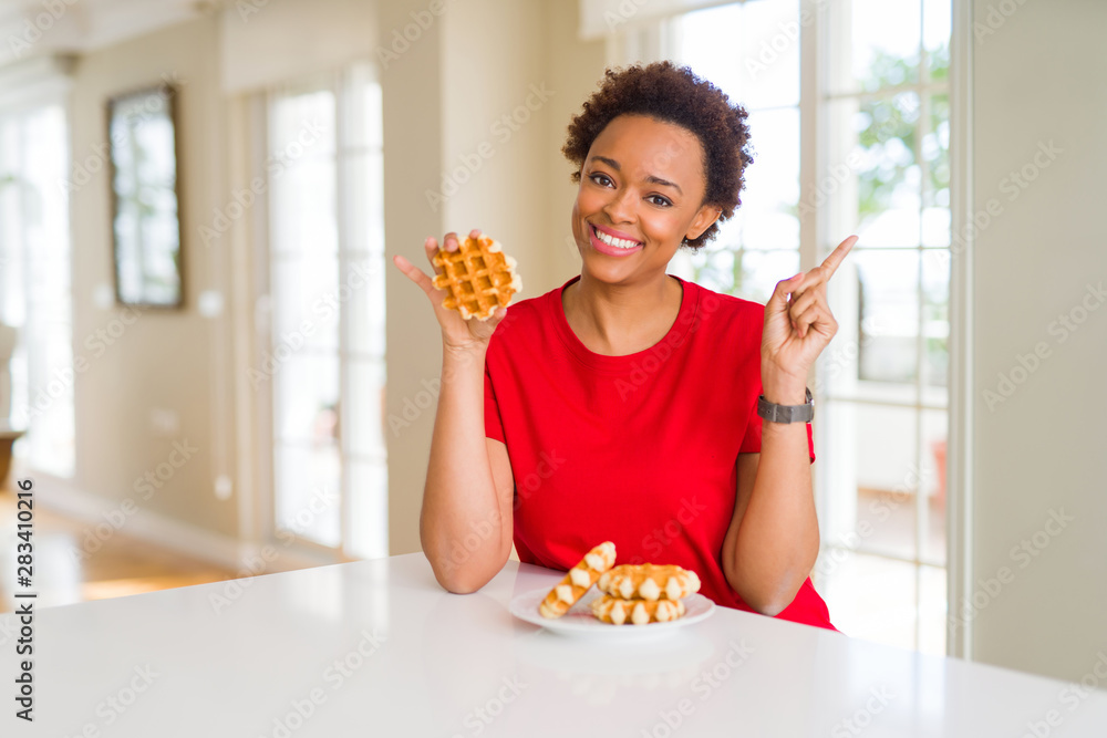 Young african american woman eating sweet waffle very happy pointing with hand and finger to the side Young african american woman eating sweet waffle very happy pointing with hand and finger to the side