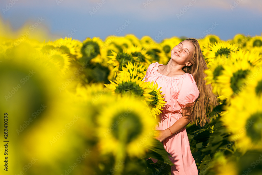 Pretty teen girl standing among sunflowers, posing for camera with eyes closed Pretty teen girl standing among sunflowers, posing for camera with eyes closed