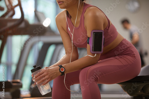 Mid section portrait of young sportswoman taking break in gym focus on smartphone in arm holder, copy space