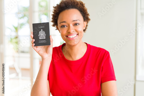 Young african american woman holding Canadian passport with a happy face standing and smiling with a confident smile showing teeth