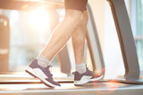 Sports background of unrecognizable man running on treadmill in gym lit by sunlight, copy space