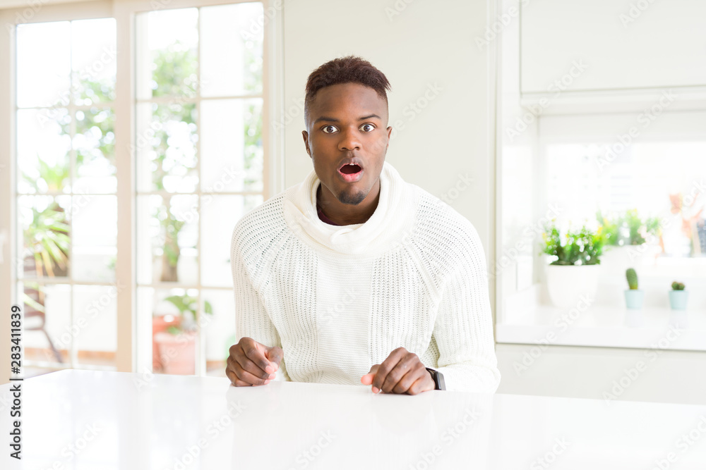 Handsome african american man on white table afraid and shocked with surprise expression, fear and excited face. Handsome african american man on white table afraid and shocked with surprise expression, fear and excited face.