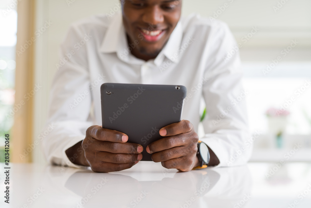 Close up of african business man using touchpad tablet, working sitting on a desk smiling Close up of african business man using touchpad tablet, working sitting on a desk smiling