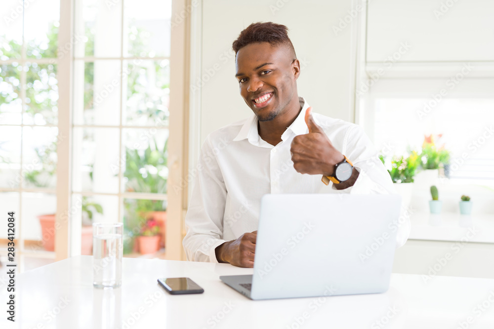 African american business man working using laptop doing happy thumbs up gesture with hand. Approving expression looking at the camera with showing success.