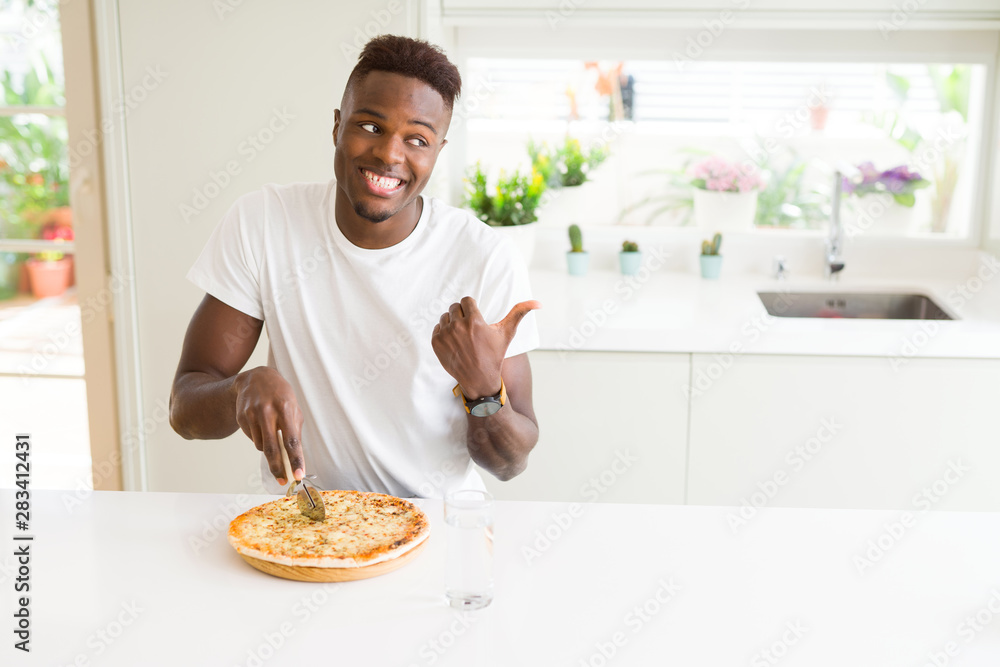 African american man eating cheese pizza at home pointing and showing with thumb up to the side with happy face smiling African american man eating cheese pizza at home pointing and showing with thumb up to the side with happy face smiling