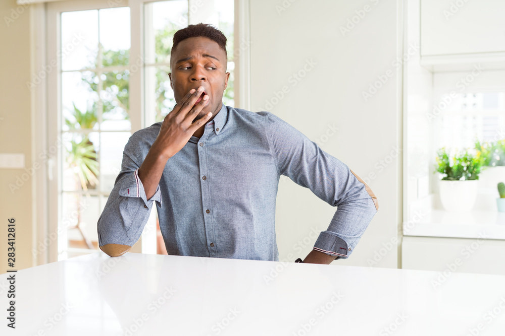 Handsome african american man on white table bored yawning tired covering mouth with hand. Restless and sleepiness. Handsome african american man on white table bored yawning tired covering mouth with hand. Restless and sleepiness.