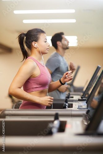 Side view portrait of people running on treadmills in gym and listening to music, copy space