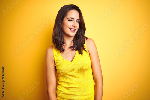 Young beautiful woman wearing t-shirt standing over yellow isolated background winking looking at the camera with sexy expression, cheerful and happy face.