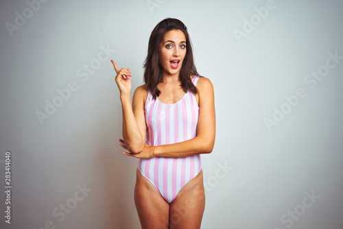 Young beautiful woman wearing striped pink swimsuit swimwear over isolated background with a big smile on face  pointing with hand finger to the side looking at the camera.