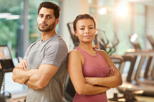Waist up portrait of beautiful mixed race couple posing confidently in gym standing with arms crossed, copy space