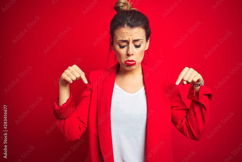 Young beautiful business woman standing over red isolated background Pointing down looking sad and upset, indicating direction with fingers, unhappy and depressed. Young beautiful business woman standing over red isolated background Pointing down looking sad and upset, indicating direction with fingers, unhappy and depressed.