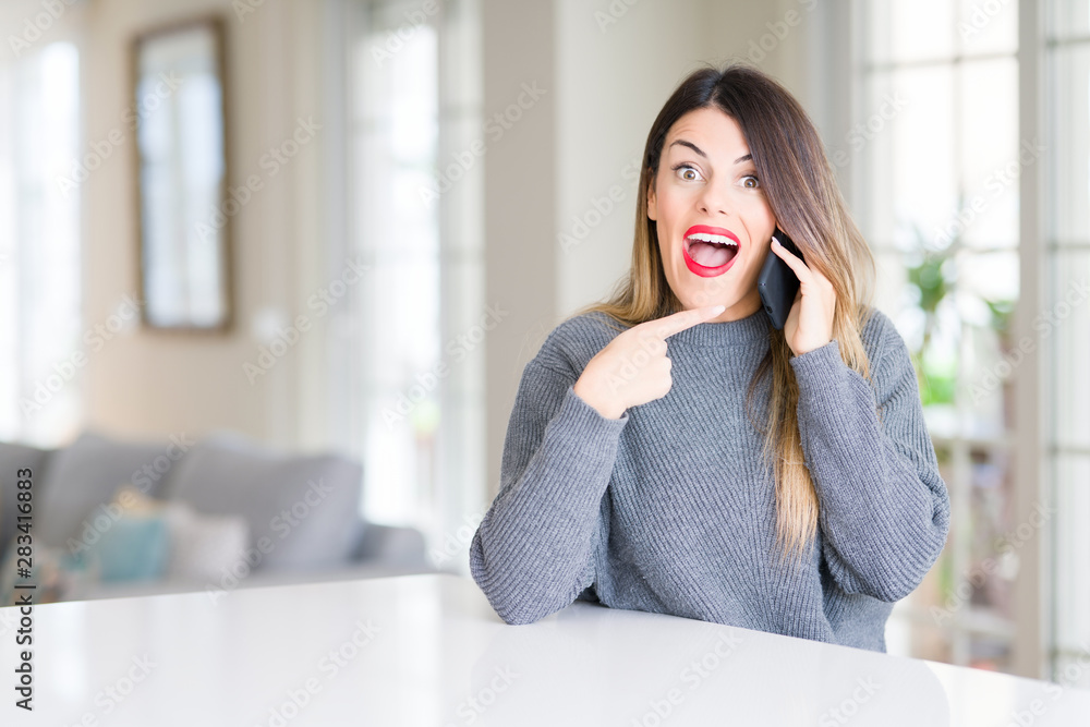 Young beautiful woman talking on the phone at home very happy pointing with hand and finger Young beautiful woman talking on the phone at home very happy pointing with hand and finger