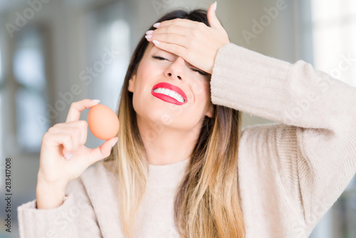 Young beautiful woman holding fresh egg at home stressed with hand on head, shocked with shame and surprise face, angry and frustrated. Fear and upset for mistake.