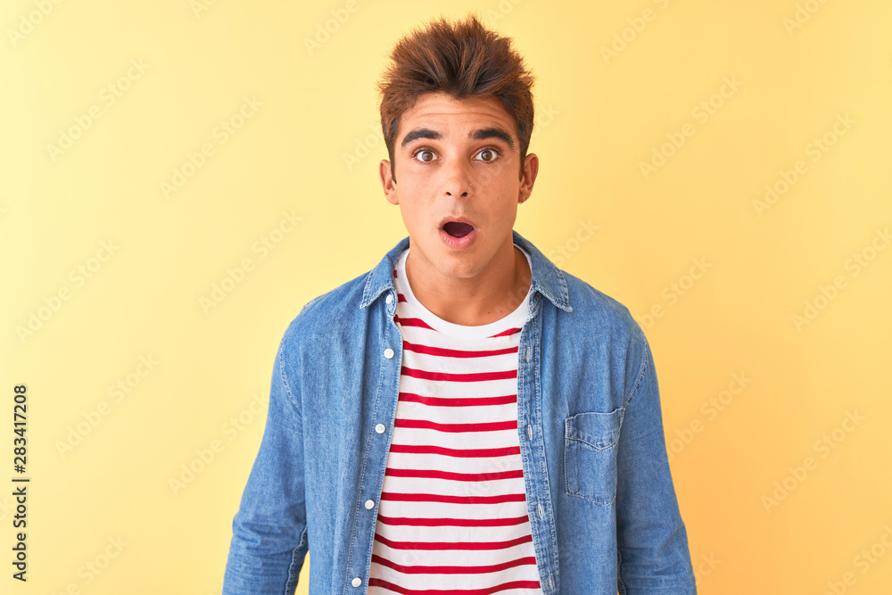 Young handsome man wearing striped t-shirt and denim shirt over isolated yellow background afraid and shocked with surprise expression, fear and excited face. Young handsome man wearing striped t-shirt and denim shirt over isolated yellow background afraid and shocked with surprise expression, fear and excited face.