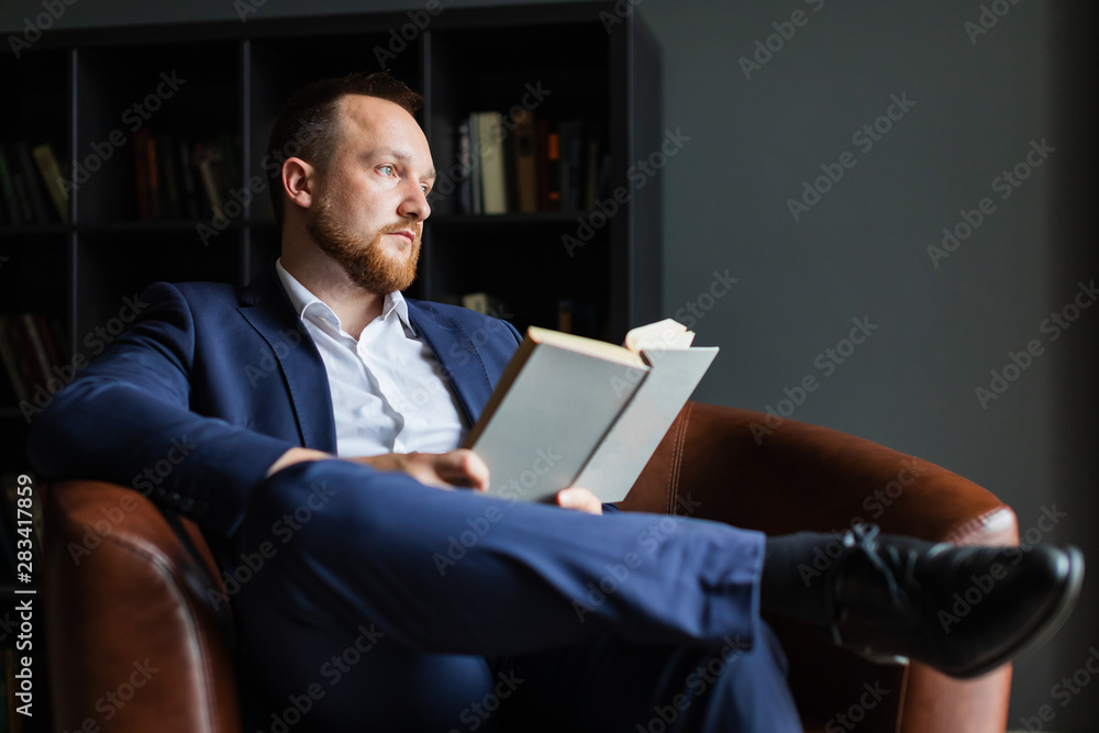 Successful businessman in a suit sits reading a book and thinks over. Successful businessman in a suit sits reading a book and thinks over.