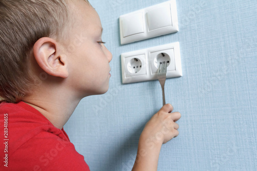 Child put fork in electric socket. Dangerous situation at home. Little boy playing with electrical outlet
