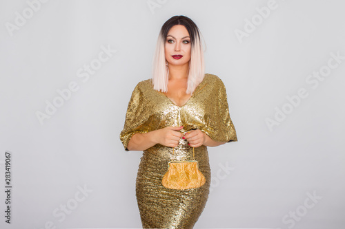 Charming young blonde haired woman wearing elegant gold evening dress and holding gold color clutch in her hands