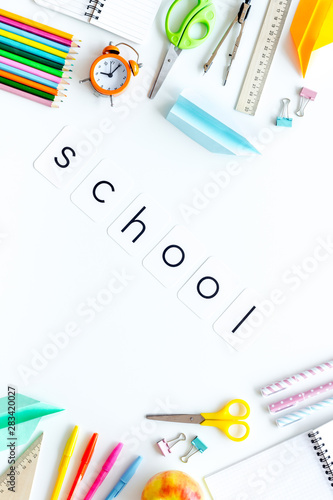Education concept with school word and frame of stationery with notebook, pens, clock on white background top view