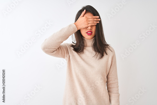 Beautiful chinese woman wearing turtleneck sweater standing over isolated white background covering eyes with hand, looking serious and sad. Sightless, hiding and rejection concept